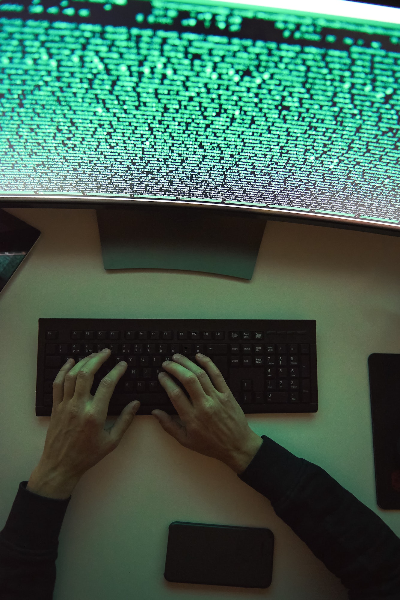 Data security. Top view of young hacker's hands stealing data while sitting in front of monitor